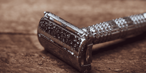 Close-up of a shiny safety razor with water droplets on its surface, placed on a wooden background. This image is perfect for discussing how often you should change your razor blades