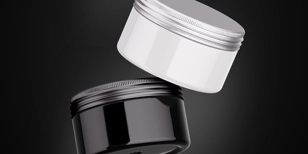 Close-up image of open tins of hair styling products, featuring pomade, wax, and clay on a wooden surface. Highlights the differences in texture and appearance between pomade vs wax vs clay.