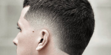 Side profile of a man with a stylish burst fade haircut. The hairstyle features a sharp, clean fade that gradually tapers down the sides and back, creating a rounded 