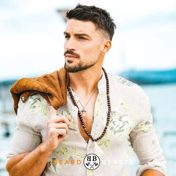 Fashionable man with styled Van Dyke Beard wearing a light floral shirt and brown jacket, accessorized with beads