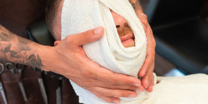 A man enjoying the benefits of a hot towel shave at a barbershop, with a warm towel wrapped around his face, ensuring a luxurious and close shave.