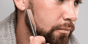 Close-up of a man skillfully using a straight razor to shave his beard, demonstrating precision and technique in traditional shaving. Learn how to shave with a straight razor for a smooth and close shave.