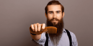 Bearded man holding a quality wooden beard comb, showcasing proper grooming tools for beard care. Learn how to comb your beard effectively with the right techniques and tools