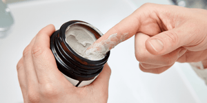 Close-up of a person scooping a dime-sized amount of hair clay from a jar, illustrating what is hair clay and how to use hair clay effectively. 