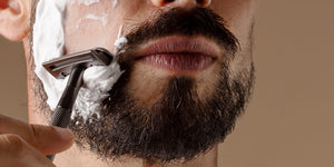 Close-up of a man shaving after comparing shaving soap vs shaving cream with a safety razor and shaving cream, showcasing the smooth application. 