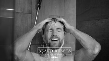 A man joyfully washing his hair in the shower, illustrating a routine for male grooming and hair care with an emphasis on determining how often should men wash their hair.