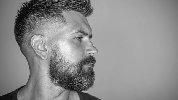 Man showcasing a modern hairstyle with a bald fade haircut, side view against a grey background, exemplifying the difference between bald fade vs skin fade styles