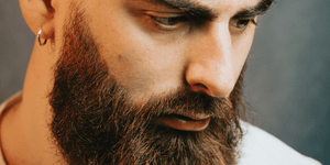 Close-up of a man with a well-groomed, thick beard and an earring, highlighting popular beard styles. Perfect example of beard grooming and maintenance for achieving stylish and healthy facial hair.