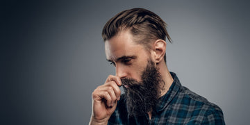 Man with a stylish slicked back haircut and a full beard, wearing a plaid shirt, looking thoughtful. Ideal example of a modern, sophisticated slicked back hairstyle for men in 2024.
