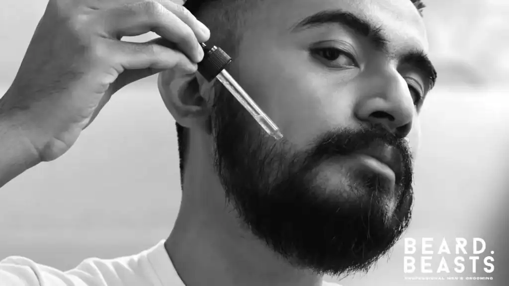 Close-up of a man using a dropper to apply beard oil directly to the skin beneath his facial hair to hydrate and prevent beard itch.