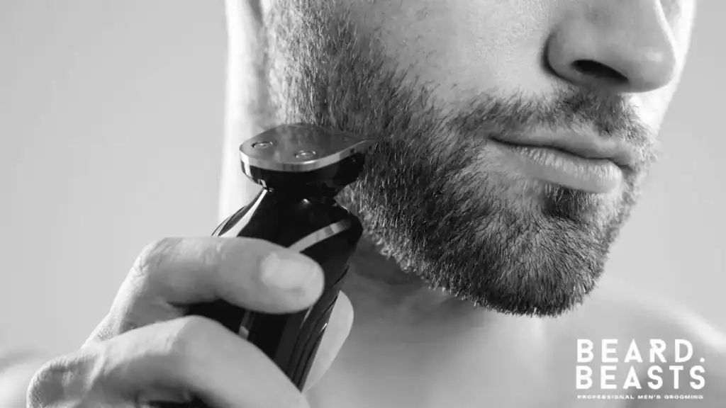 Close-up of a man using an electric beard trimmer to define a sharp cheek line and control beard density for a structured look.
