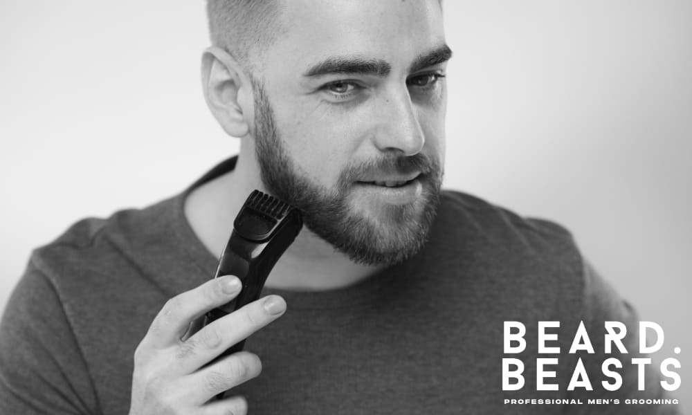 Man trimming his short beard with an electric trimmer, demonstrating technique for a clean and even grooming result.