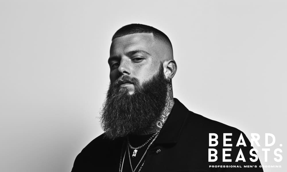 Serious-looking man with a full, well-groomed beard and sharp buzz cut—capturing the confidence and discipline behind true beard commitment.