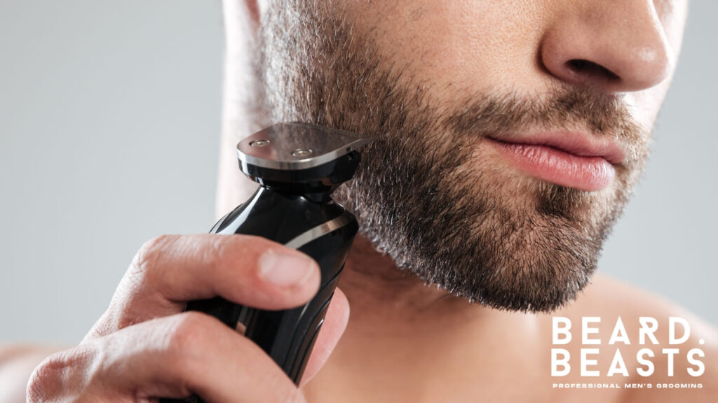 A close-up of a bearded man using an electric beard trimmer to shape and maintain his facial hair.