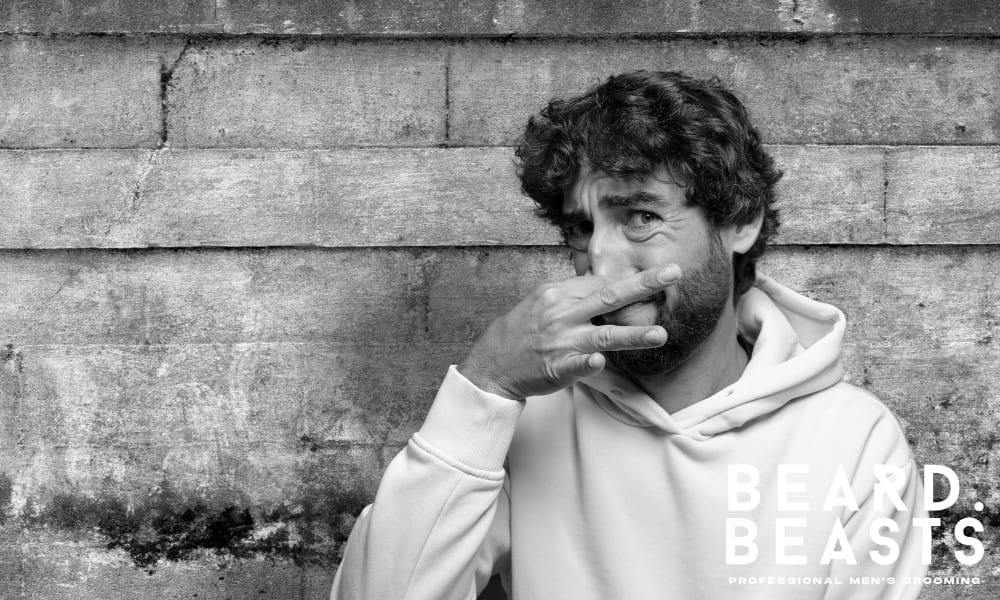Man holding his nose in disgust to avoid a bad smell, illustrating the consequences of skipping beard washes and poor beard hygiene.