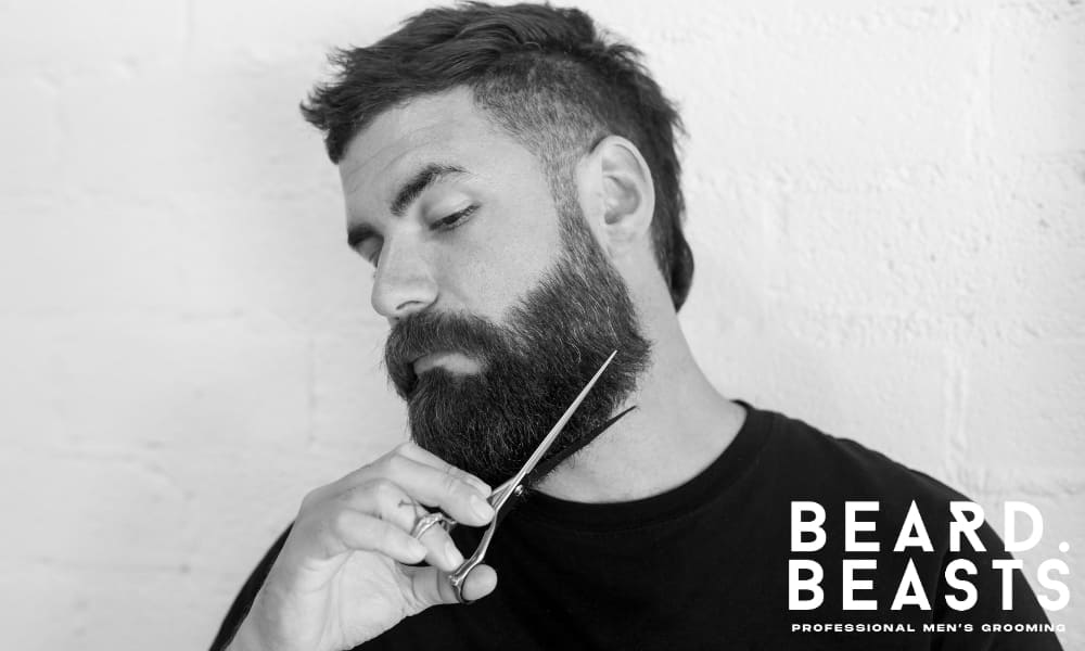 Close-up of a man trimming his beard with scissors, demonstrating the proper technique for regular beard trimming to maintain softness and shape.