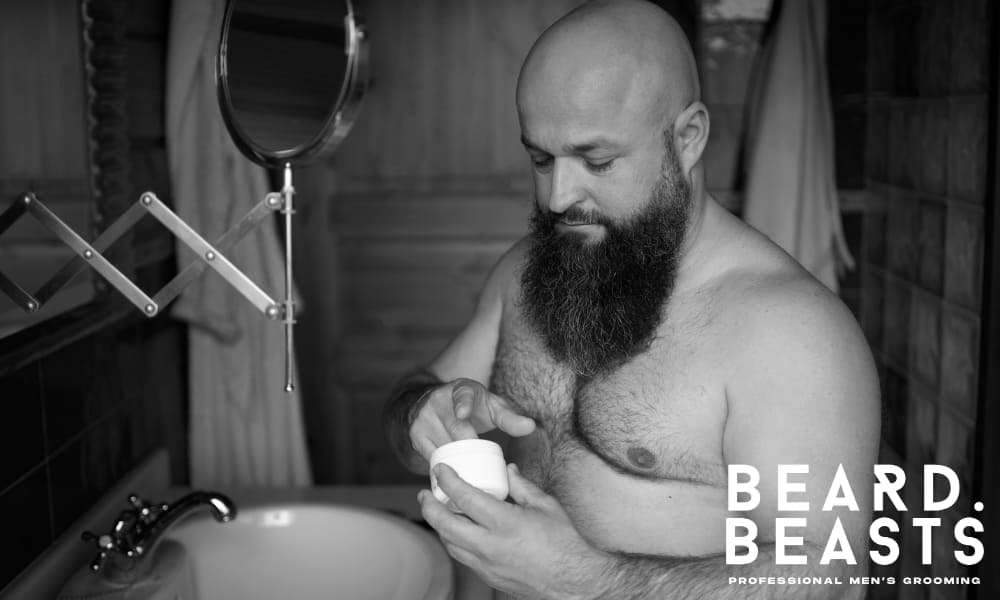 Bearded man applying beard balm in a bathroom, highlighting proper grooming routine and ideal timing after showering for maximum effectiveness.