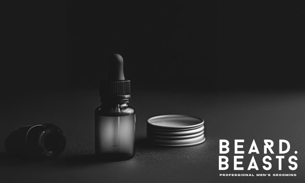 Moody black and white image of a beard oil bottle and a tin of beard butter on a dark surface, emphasizing premium grooming products from Beard Beasts.