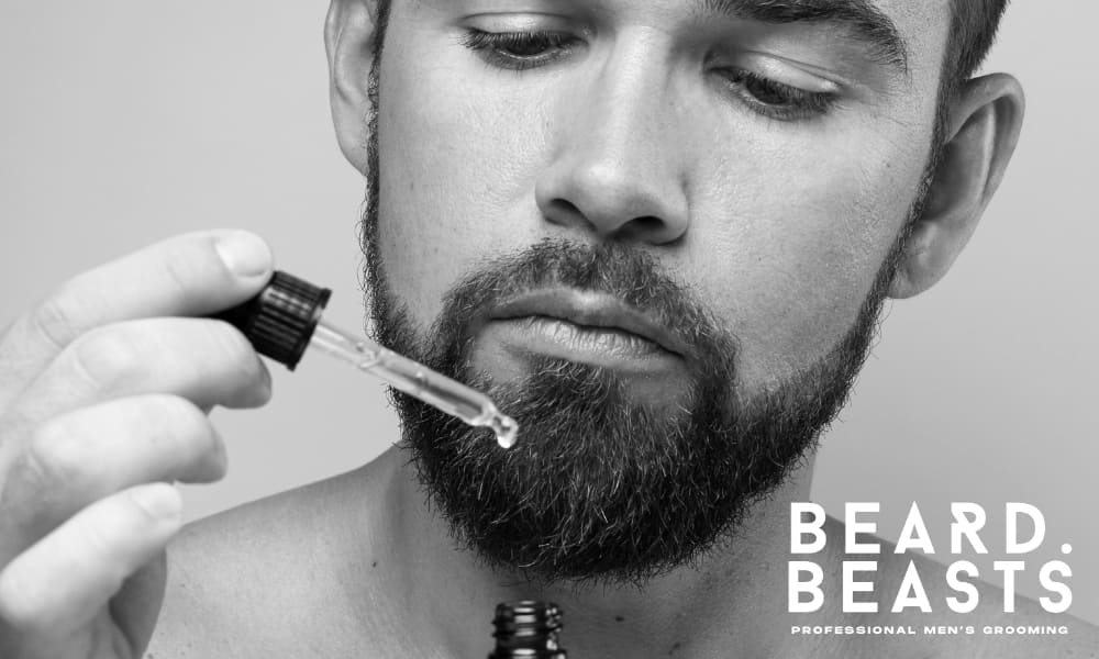 Close-up image of a man applying beard oil to his beard, addressing common concerns like 'why does my beard hurt' and 'beard pain.' The image highlights the importance of proper beard care and hydration to reduce discomfort, with the Beard Beasts logo emphasizing professional grooming solutions.