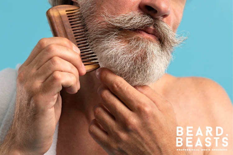 A mature man with a well-groomed gray beard and mustache, using a grooming tool to style and maintain his beard. The image highlights the importance of proper beard care for a polished and professional appearance.