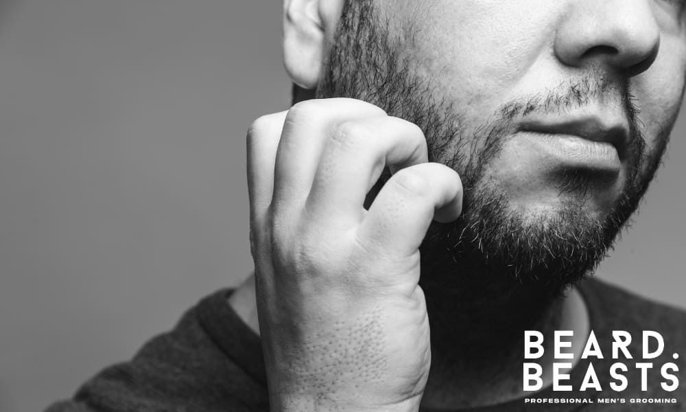 Close-up of a man scratching his beard, showing signs of persistent dry skin, irritation, or underlying skin conditions