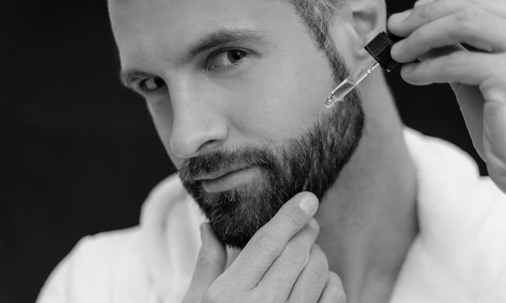 Close-up of a man applying beard oil with a dropper to treat a dry beard—hydrating and nourishing facial hair for healthier growth.