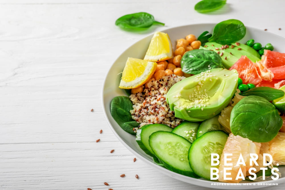 A colorful plate of nutrient-rich food, featuring fresh avocado, cucumber slices, spinach leaves, quinoa, chickpeas, lemon wedges, and grapefruit segments. The ingredients are carefully arranged, emphasizing a healthy, balanced diet ideal for promoting beard growth.