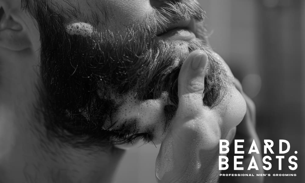 Black and white close-up of a man washing his beard with foamy lather, gently massaging the hair to promote cleanliness and hydration. The well-defined beard showcases the importance of proper grooming techniques to prevent issues like beard hair sticking out.