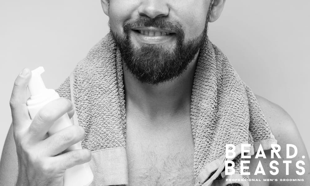 Man with a towel and healthy beard applying skincare product to support beard growth.
