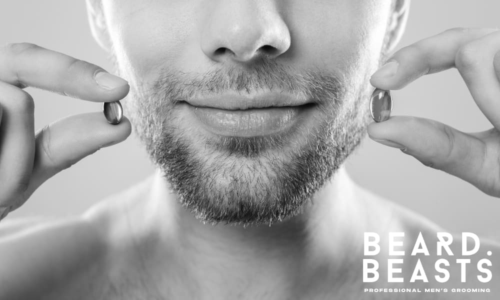 Close-up of a man with a short beard holding two supplement capsules, highlighting the role of vitamins in beard growth.