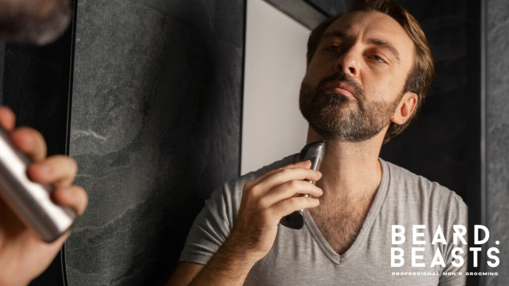 A bearded man using a trimmer to carefully shave his neckline in front of a mirror. The image demonstrates proper grooming techniques for maintaining a clean and defined neckline while growing a beard.