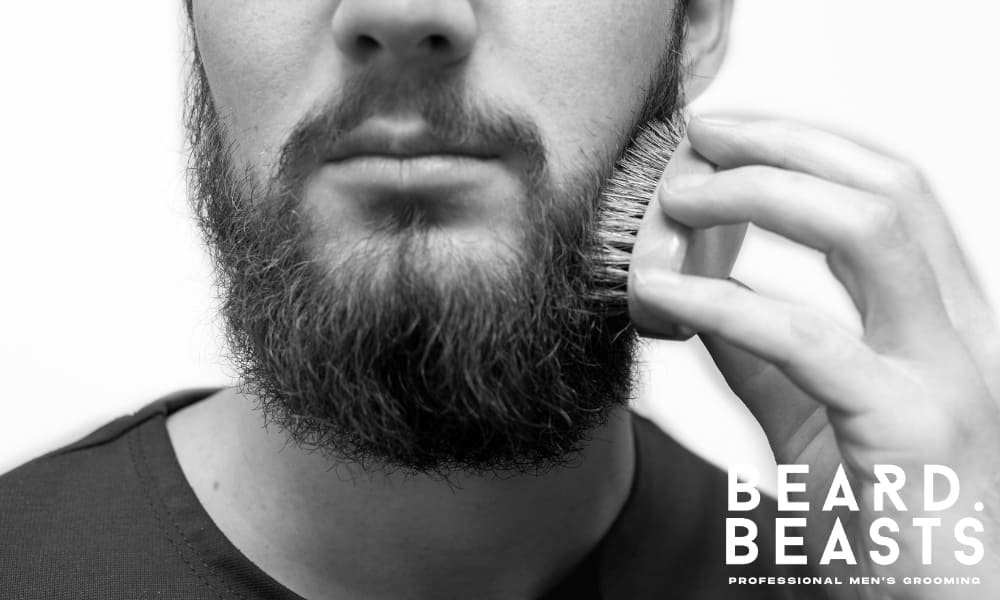 Man brushing his beard with a boar bristle brush to train growth direction and promote healthier beard growth.