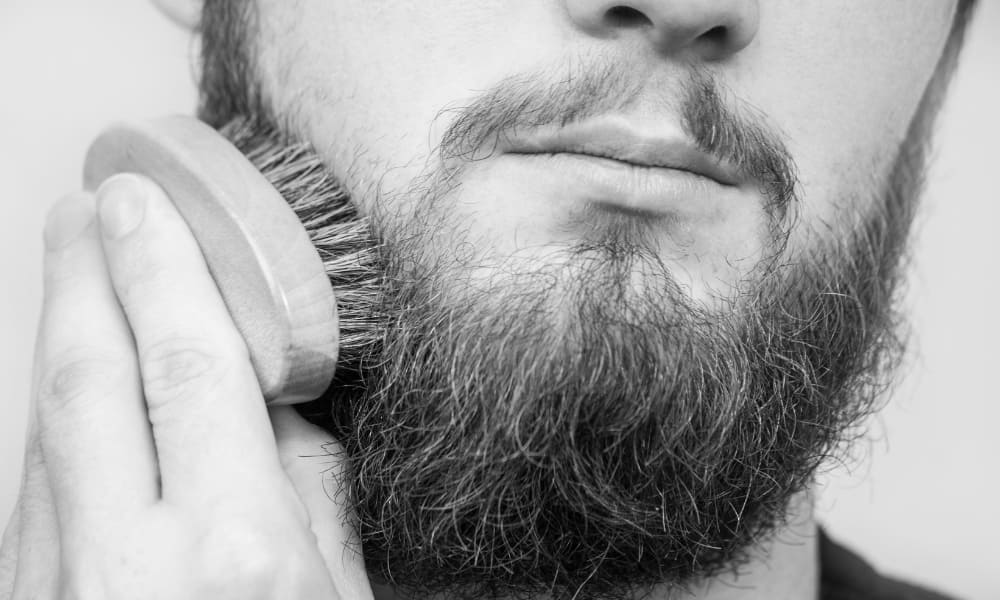 Close-up of a man brushing his full beard with a boar bristle beard brush, highlighting proper grooming technique and beard care.