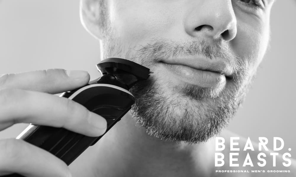 A man trimming his beard with an electric trimmer — a key tool for how to trim a beard while growing it out.