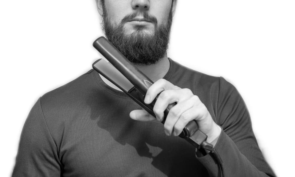 Close-up of a man holding a heated beard straightener, illustrating overengineered beard grooming tools that are often unnecessary.