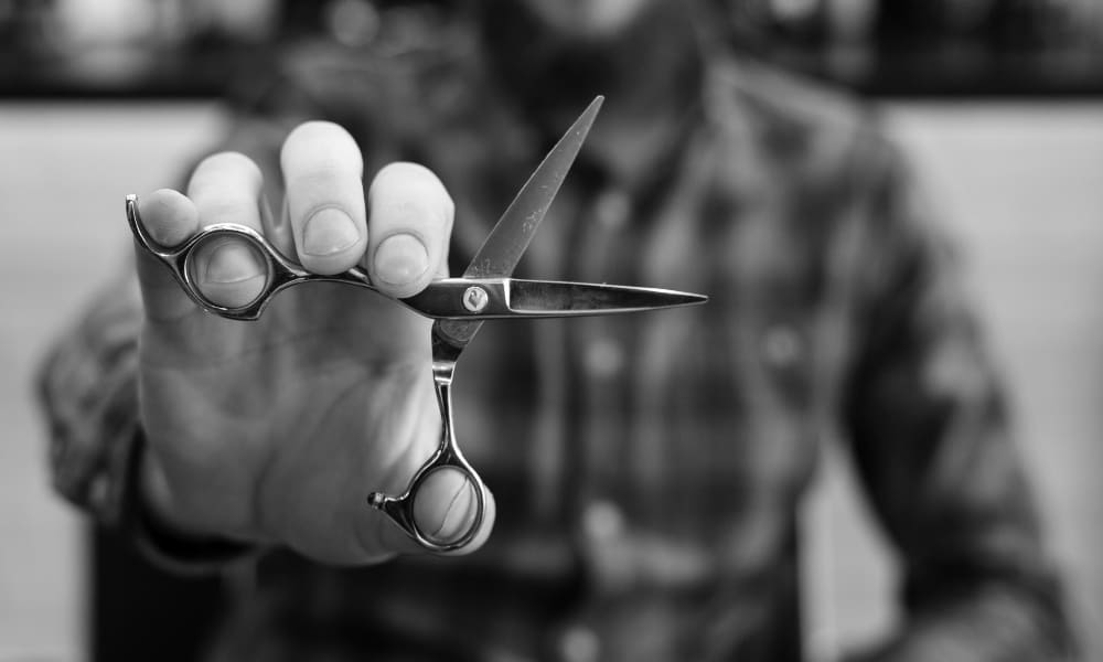 Close-up of a man holding professional beard trimming scissors in a barbershop, emphasizing precision grooming tools for beards.