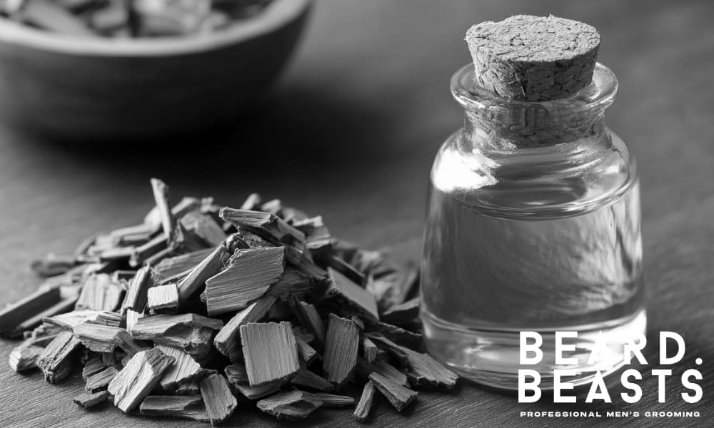 Glass bottle of cedarwood essential oil with cedarwood chips on a wooden surface—used to strengthen hair roots and support beard growth.