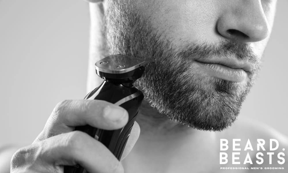Close-up of a man trimming an overgrown beard with an electric trimmer—highlighting a common mistake of letting stubble exceed ideal length and lose its defined structure.