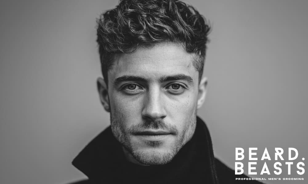 Close-up black and white portrait of a man with designer stubble—clean neckline, defined cheek lines, and evenly trimmed facial hair for a sharp, structured look.