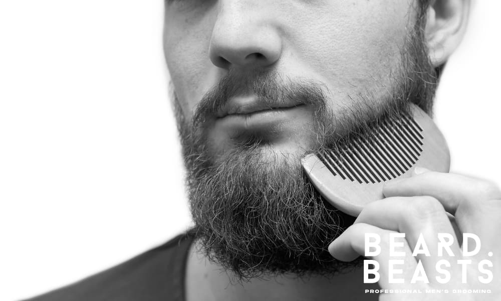 Close-up of man combing his beard with a wooden comb to reduce tangles, train growth direction, and support daily beard upkeep.