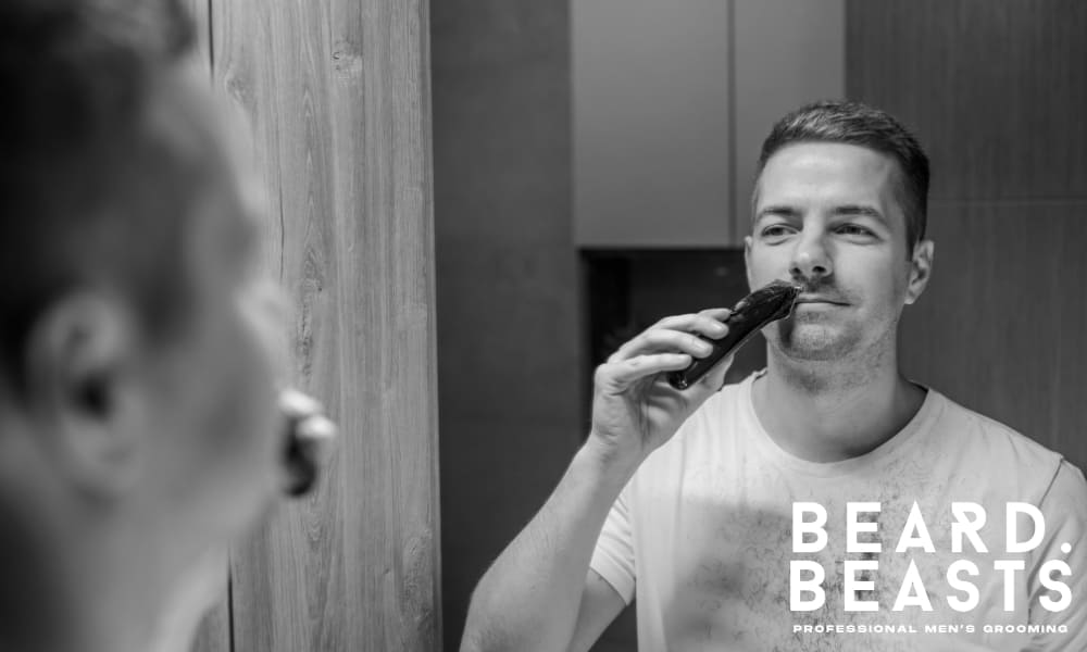 Man trimming his 4mm beard in front of the bathroom mirror with an electric trimmer.