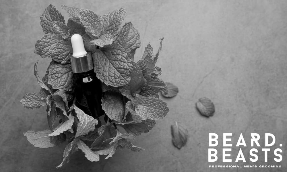 Dark glass dropper bottle surrounded by fresh peppermint leaves—used to stimulate blood flow and support beard growth naturally.