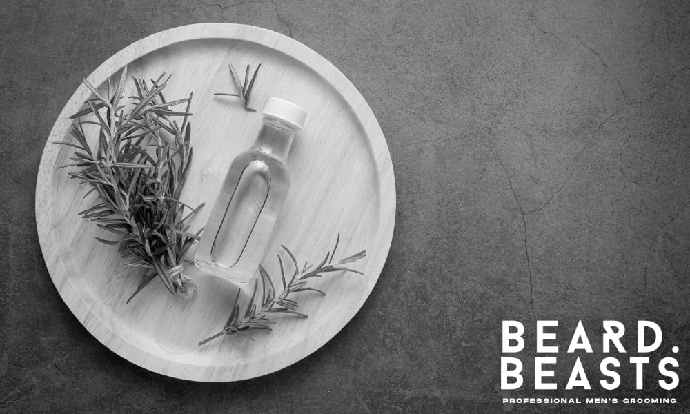 Bottle of rosemary oil with fresh rosemary sprigs on a wooden plate—used to boost circulation and support facial hair growth naturally.