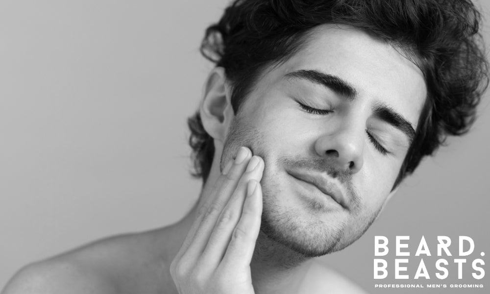 Man gently touching his very short facial hair-covered face with eyes closed, showing healthy skin and proper care after grooming.
