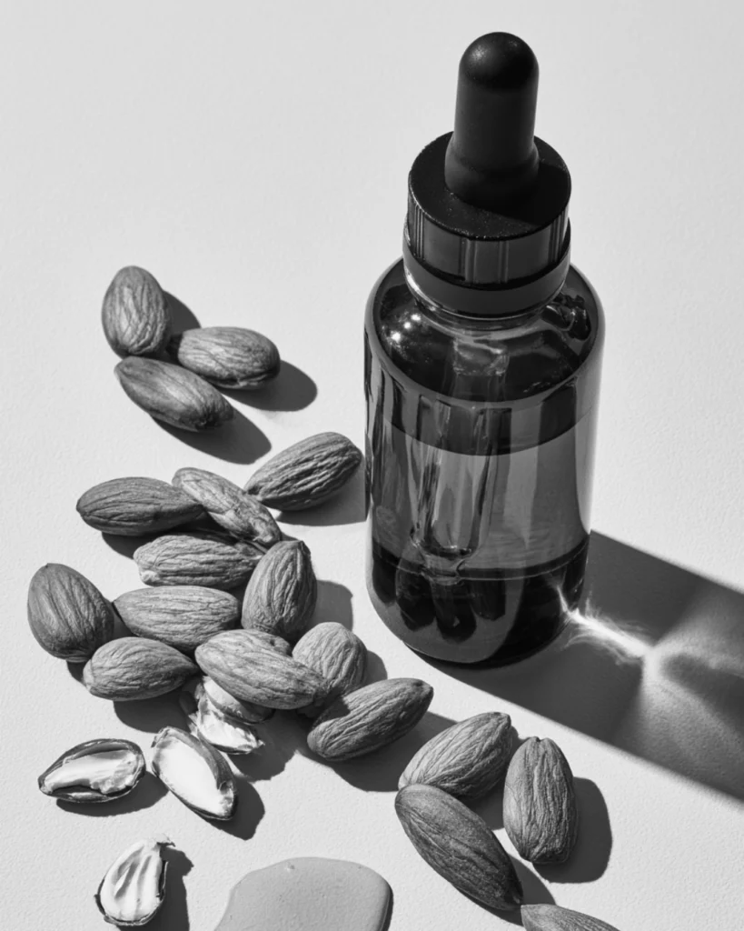 Amber dropper bottle of sweet almond oil surrounded by almonds for use in beard care