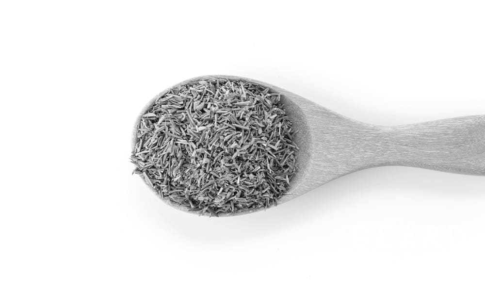 Dried thyme in a wooden spoon on a white background—commonly used in oil blends for natural beard care.