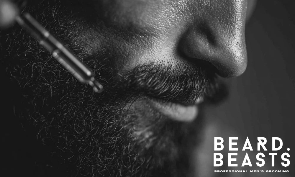 Close-up of a man applying jojoba oil to his beard using a dropper, highlighting beard texture and skincare routine