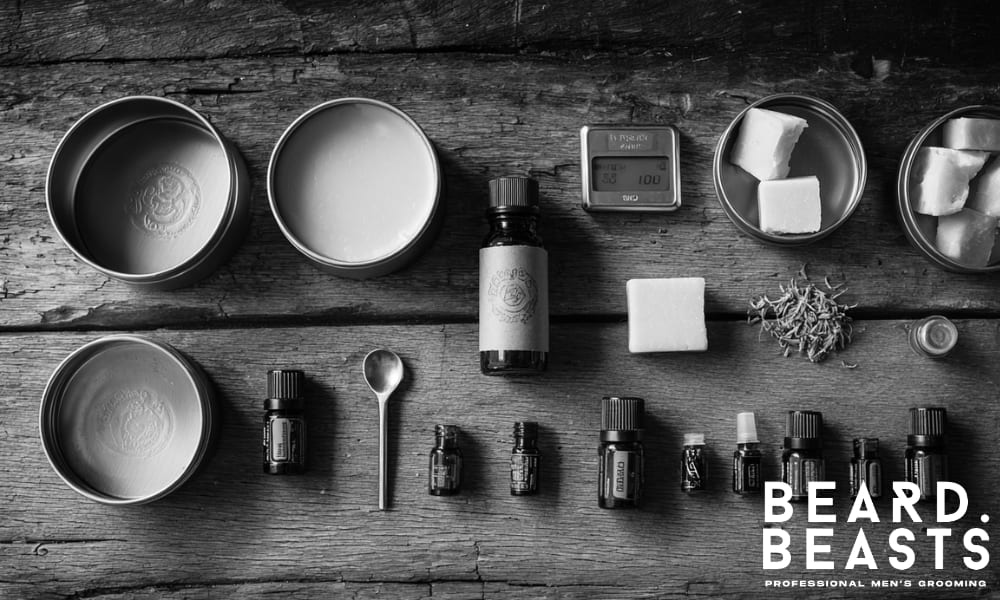 flat lay of beard balm making tools including tins, butters, essential oils, scale, and spoon on rustic wooden surface
