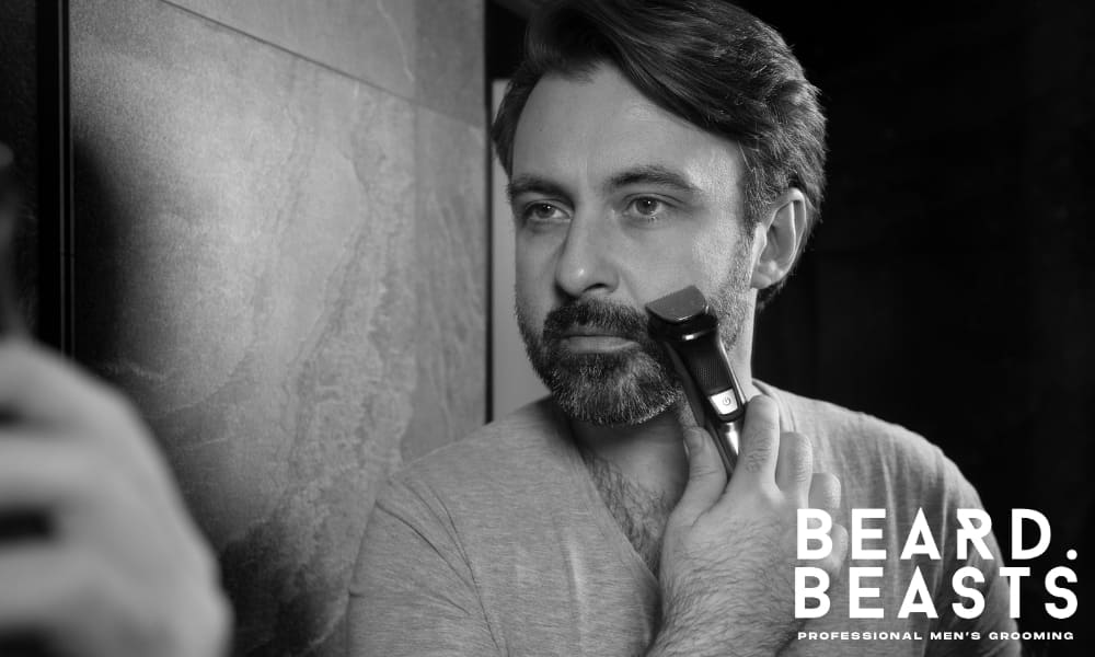 Man trimming his beard in the mirror as part of his grooming routine for learning how to grow a full beard