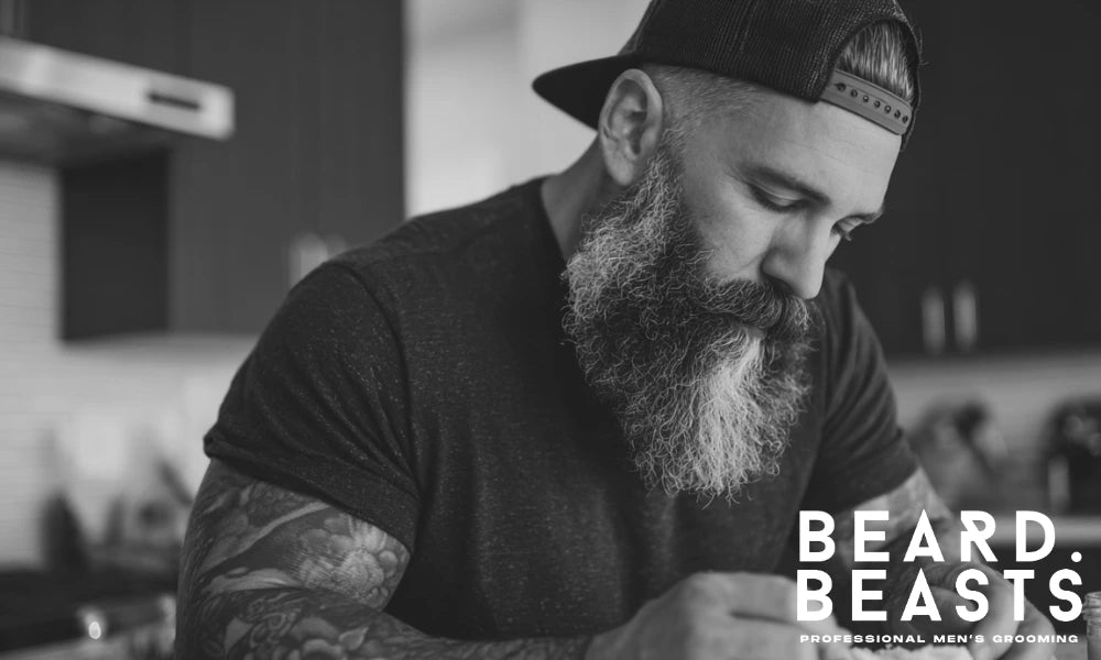 Bearded man in a kitchen preparing homemade beard butter, focused on the mixing process.